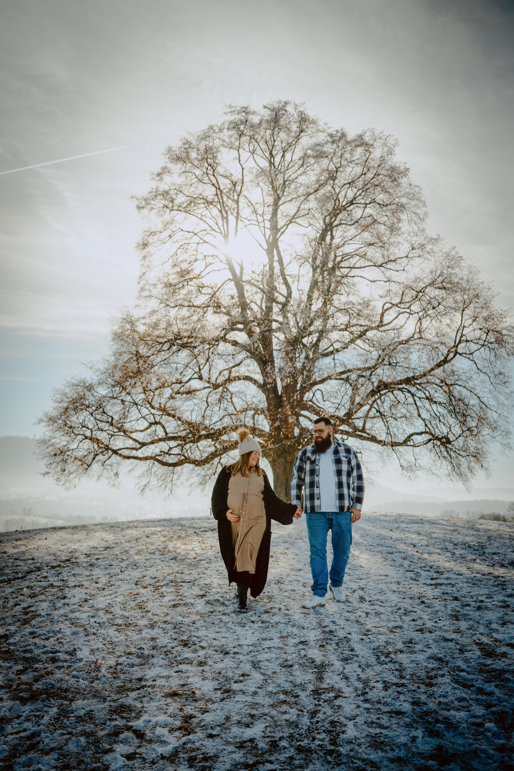 Schwangere läuft über eine schneebdeckte Wiese mit Sonne im Hintergrund
